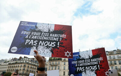 Des manifestants tenant des pancartes sur lesquelles on peut lire "Vous vous habituez à l'antisémitisme, pas nous", lors d'un rassemblement pour condamner le viol collectif antisémite d'une jeune fille de 12 ans, devant l'Hôtel de ville de Paris, le 19 juin 2024. (Crédit : Alain Jocard/AFP)
