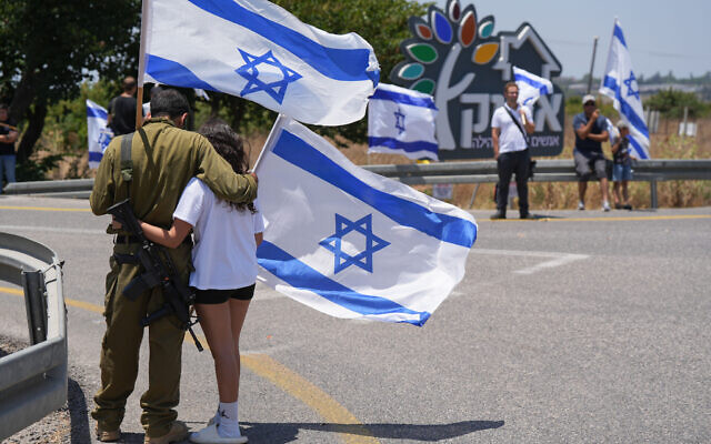 Des personnes à l'extérieur du kibboutz Afik agitant des drapeaux alors qu'elles rendent un dernier hommage au sergent Eyal Shynes, tué à Gaza, le 28 juin 2024. (Crédit : Ayal Margolin/Flash90) Des personnes à l'extérieur du kibboutz Afik agitant des drapeaux alors qu'elles rendent un dernier hommage au sergent Eyal Shynes, tué à Gaza, le 28 juin 2024. (Crédit : Ayal Margolin/Flash90)