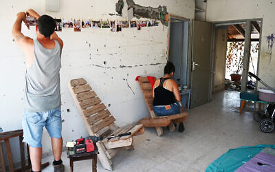 Ido Vered-Bar accroche des photos de famille dans la maison des parents assassinés de sa femme Noya, à droite, dans le kibboutz Beeri, le 10 juillet 2024. (Crédit : Canaan Lidor/Times of Israel)