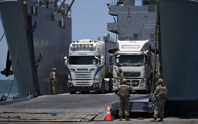 Des soldats de l'armée américaine font un geste alors que des camions chargés d'aide humanitaire arrivent à l'embarcadère flottant Trident construit par les États-Unis avant d'atteindre la plage sur la côte de la bande de Gaza, le 25 juin 2024. (Crédit : Leo Correa/AP)