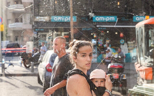 Une femme portant un bébé passe devant des éclats de verre au lendemain d'une explosion qui s'est produite à Tel Aviv le 19 juillet 2024. (Crédit : GIL COHEN-MAGEN / AFP)