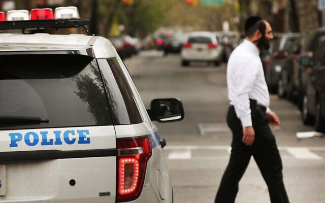 Un homme hassidique passant devant une voiture de police dans un quartier juif orthodoxe de Brooklyn, le 24 avril 2017. (Crédit : Spencer Platt/Getty Images via JTA)