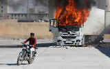 Un homme conduisant une moto près d'un camion turc en feu lors de manifestations contre la Turquie à al-Bab, dans la région d'Alep, au nord de la Syrie, tenue par l'opposition, le 1er juillet 2024. (Crédit : Bakr Alkasem/AFP)