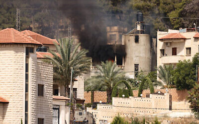 Un véhicule militaire israélien devant un bâtiment en feu, lors d'un raid israélien à Jénine, en Cisjordanie, le 5 juillet 2024. (Crédit : Jaafar Ashtiyeh/ AFP)