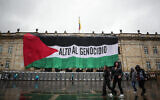 Des passants devant un drapeau palestinien géant sur lequel est écrit en espagnol « Stop au génocide » couvrant la façade du bâtiment du Congrès colombien, à Bogota, le 5 juillet 2024. (Crédit : Pablo Pino/AFP)