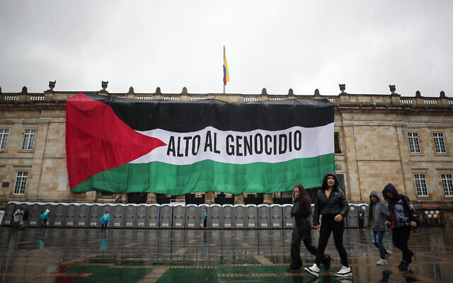 Des passants devant un drapeau palestinien géant sur lequel est écrit en espagnol « Stop au génocide » couvrant la façade du bâtiment du Congrès colombien, à Bogota, le 5 juillet 2024. (Crédit : Pablo Pino/AFP) Des passants devant un drapeau palestinien géant sur lequel est écrit en espagnol « Stop au génocide » couvrant la façade du bâtiment du Congrès colombien, à Bogota, le 5 juillet 2024. (Crédit : Pablo Pino/AFP)