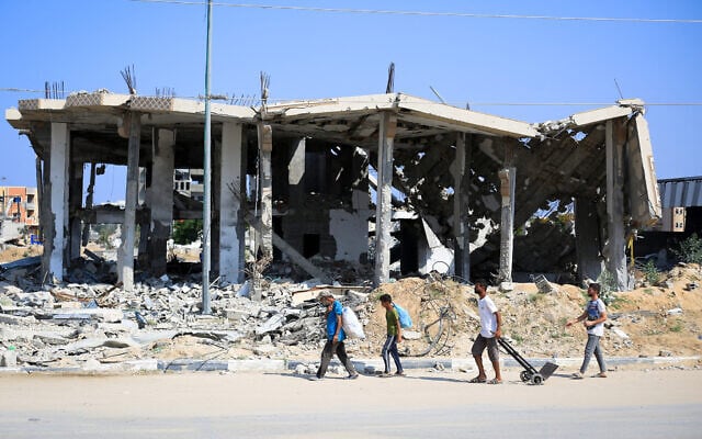 Des Palestiniens transportant leurs effets personnels devant un bâtiment détruit de Deir el-Balah, dans le centre de la bande de Gaza, le 7 juillet 2024. (Crédit : Eyad Baba/AFP) Des Palestiniens transportant leurs effets personnels devant un bâtiment détruit de Deir el-Balah, dans le centre de la bande de Gaza, le 7 juillet 2024. (Crédit : Eyad Baba/AFP)