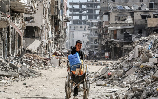 Un garçon pousse un fauteuil roulant transportant des bidons d'eau devant les décombres de bâtiments détruits dans une rue de Khan Younès, dans le sud de la bande de Gaza, le 8 juillet 2024. (Crédit : Bashar Taleb/AFP) Un garçon pousse un fauteuil roulant transportant des bidons d'eau devant les décombres de bâtiments détruits dans une rue de Khan Younès, dans le sud de la bande de Gaza, le 8 juillet 2024. (Crédit : Bashar Taleb/AFP)