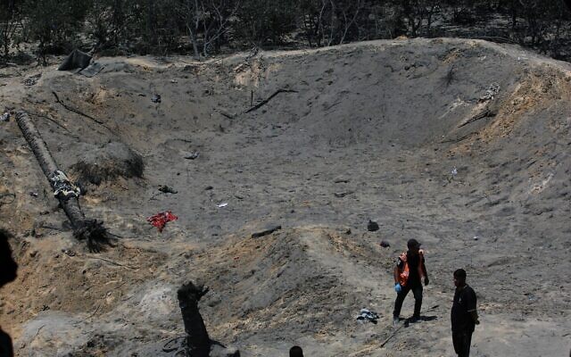 Des Palestiniens observant un énorme cratère dans le sable après une frappe militaire israélienne près de la ville de Khan Younès, dans le sud de la bande de Gaza, le 13 juillet 2024. (Crédit : Bashar Taleb/AFP) Des Palestiniens observant un énorme cratère dans le sable après une frappe militaire israélienne près de la ville de Khan Younès, dans le sud de la bande de Gaza, le 13 juillet 2024. (Crédit : Bashar Taleb/AFP)