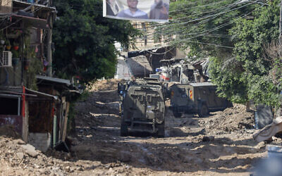 Des véhicules militaires israéliens traversent une route creusée par l'armée pour désactiver les explosifs cachés, lors d'un raid à Tulkarem en Cisjordanie, le 23 juillet 2024. (Crédit : JAAFAR ASHTIYEH / AFP)
