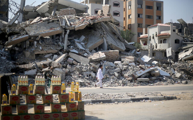 Un homme passe devant un étalage de bouteilles installé par un vendeur près de bâtiments détruits lors d'un précédent bombardement israélien à Bureij, dans le centre de la bande de Gaza, le 28 juillet 2024. (Crédit : Eyad Baba/AFP)