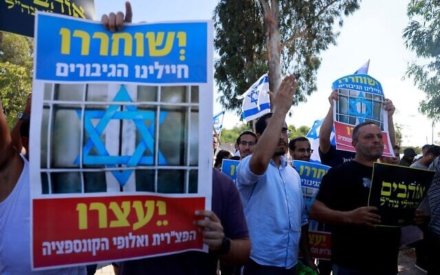 Des manifestants tenant des affiches sur laquelle on peut lire « Nos héroïques soldats devraient être libérés », protestant contre la détention de réservistes soupçonnés d'avoir sévèrement maltraité un terroriste palestinien présumé, devant un tribunal militaire de la base militaire de Beit Lid, à proximité de Kfar Yona, le 30 juillet 2024. (Crédit : Menahem Kahana/AFP)