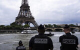 Des policiers observant les bateaux de la police fluviale patrouillant devant la Tour Eiffel, sur la Seine, à Paris, le 2 juillet 2024. (Crédit : Louise Delmotte/AP)