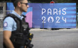 Un officier de police devant une bâche des Jeux Olympiques de Paris 2024, à Paris, le 20 juillet 2024. (Crédit : Thomas Padilla/AP)
