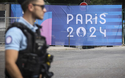 Un officier de police devant une bâche des Jeux Olympiques de Paris 2024, à Paris, le 20 juillet 2024. (Crédit : Thomas Padilla/AP)