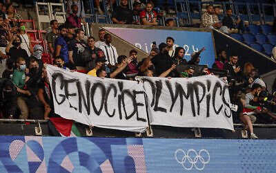 Des manifestants brandissant une banderole sur laquelle on peut lire « Les Jeux olympiques du génocide » lors du match de football entre Israël et le Paraguay, au Parc des Princes, lors des Jeux olympiques d'été de 2024, à Paris, en France, le 27 juillet 2024. (Crédit : Aurélien Morissard/AP)