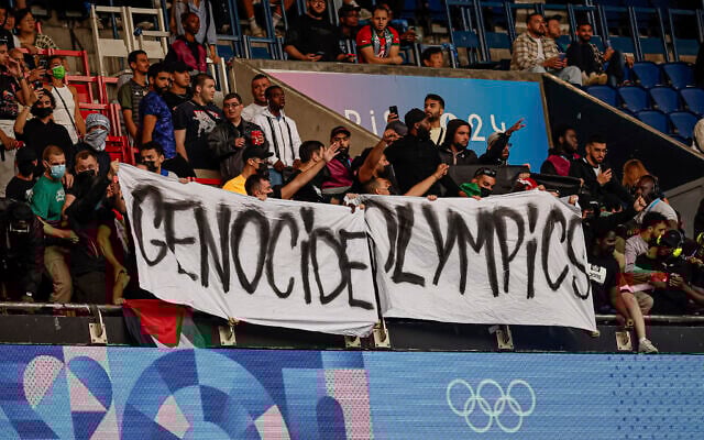Des manifestants brandissant une banderole sur laquelle on peut lire « Les Jeux olympiques du génocide » lors du match de football entre Israël et le Paraguay, au Parc des Princes, lors des Jeux olympiques d'été de 2024, à Paris, en France, le 27 juillet 2024. (Crédit : Aurélien Morissard/AP) Des manifestants brandissant une banderole sur laquelle on peut lire « Les Jeux olympiques du génocide » lors du match de football entre Israël et le Paraguay, au Parc des Princes, lors des Jeux olympiques d'été de 2024, à Paris, en France, le 27 juillet 2024. (Crédit : Aurélien Morissard/AP)
