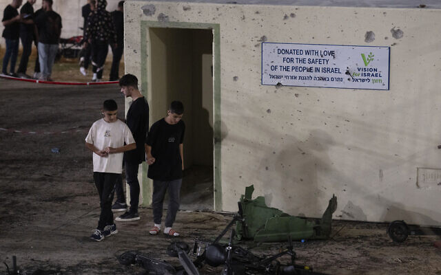 Des jeunes marchant à côté d'un abri endommagé par des éclats d'obus sur un terrain de football frappé par une roquette - une attaque qui a tué de nombreux enfants et adolescents - dans la ville druze de Majdal Shams, sur le plateau du Golan, le 27 juillet 2024. (Crédit : Leo Correa/AP) Des jeunes marchant à côté d'un abri endommagé par des éclats d'obus sur un terrain de football frappé par une roquette - une attaque qui a tué de nombreux enfants et adolescents - dans la ville druze de Majdal Shams, sur le plateau du Golan, le 27 juillet 2024. (Crédit : Leo Correa/AP)