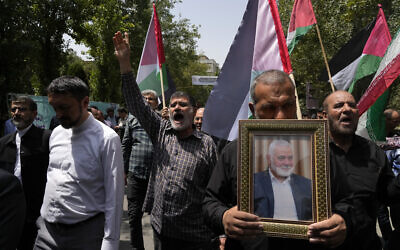 Les membres du conseil de l'Université de Téhéran lors d'une manifestation condamnant le meurtre du chef du bureau politique du Hamas, Ismaïl Haniyeh, brandissant des drapeaux iraniens et palestiniens tandis qu'une image du drapeau israélien est peinte sur le sol de l'Université, à Téhéran, le 31 juillet 2024. (Crédit : Vahid Salemi/AP)