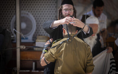 Un homme haredi plaçant des tefillin sur un soldat, dans la Vieille Ville de Jérusalem, le 25 juin 2024. (Crédit : Chaïm Goldberg/Flash90)