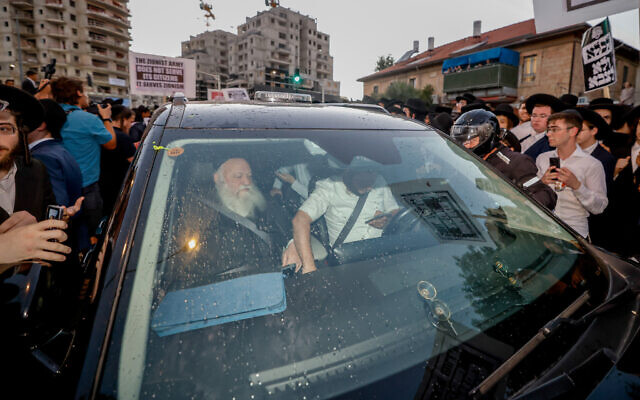 La police protégeant la voiture du ministre du Logement Yitzhak Goldknopf lors d'une manifestation contre la conscription des Haredim étudiant en yeshiva dans l'armée, dans le quartier de Mea Shearim, à Jérusalem, le 30 juin 2024. (Crédit : Chaïm Goldberg/Flash90)