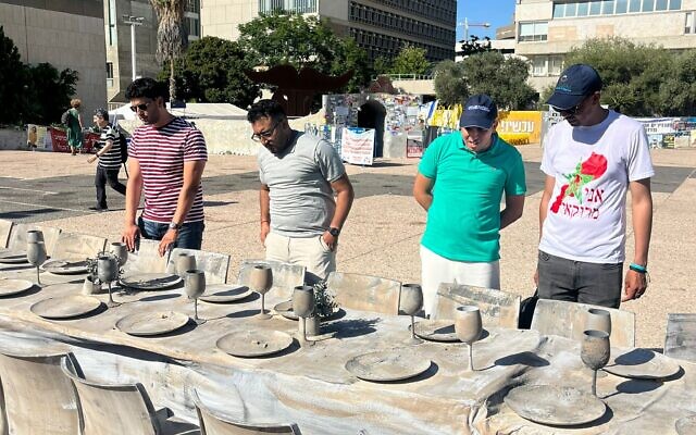 De jeunes Marocains en visite en Israël autour d'une table vide évoquant les otages détenus par le Hamas à Gaza sur la place des Otages de Tel Aviv, le 11 juillet 2024. (Autorisation : Sharaka)
