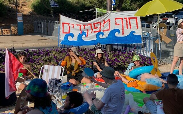Des manifestants anti-gouvernement protestent devant le bâtiment de la Knesset à Jérusalem sous une banderole intitulée "Plage des abandonnés", critiquant les vacances législatives de trois mois qui ont commencé le même jour, le 28 juillet 2024. (Crédit : Charlie Summers/Times of Israel) Des manifestants anti-gouvernement protestent devant le bâtiment de la Knesset à Jérusalem sous une banderole intitulée "Plage des abandonnés", critiquant les vacances législatives de trois mois qui ont commencé le même jour, le 28 juillet 2024. (Crédit : Charlie Summers/Times of Israel)
