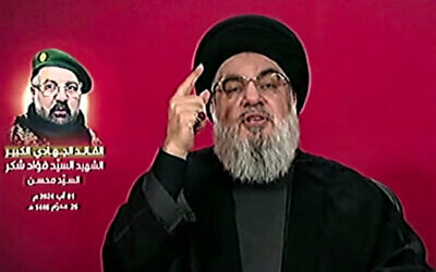 Une image prise par la chaîne de télévision al-Manar du Hezbollah le 1er août 2024 montre le chef du Hezbollah, Hassan Nasrallah, prononçant un discours télévisé depuis un lieu non divulgué au Liban, retransmis lors de la cérémonie funéraire du commandant Fuad Shukr. L'image de Shukr est sur l'écran derrière lui. (Crédit : Al-Manar/AFP)