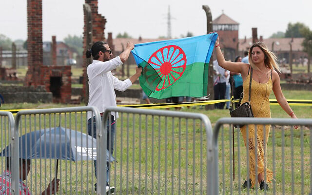 Des personnes affichent un drapeau rom pour commémorer les Roms et les Sintis tués par l'Allemagne nazie pendant la Seconde Guerre mondiale, lors de cérémonies, à Oswiecim, en Pologne, le 2 août 2019. (Crédit : Czarek Sokolowski/AP)