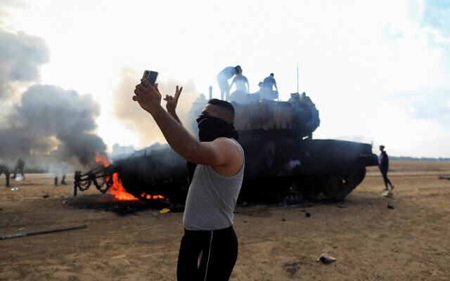 Des Gazaouis devant un véhicule militaire israélien en feu du côté israélien de la frontière entre Israël et Gaza, le 7 octobre 2023. (Crédit : Yasser Qudih/Reuters) Des Gazaouis devant un véhicule militaire israélien en feu du côté israélien de la frontière entre Israël et Gaza, le 7 octobre 2023. (Crédit : Yasser Qudih/Reuters)