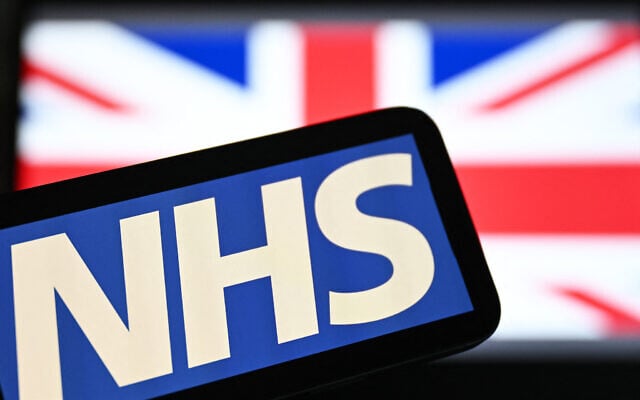 Illustration : Le logo du National Health Service (NHS) affiché sur un écran avec en toile de fond le drapeau de l'Union Jack, le 7 juillet 2024. (Crédit : Justin Tallis/AFP)