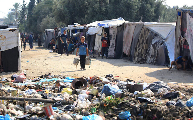 Des Palestiniens déplacés assis près de tentes, en face d'une décharge à Deir el-Balah, dans le centre de la bande de Gaza, le 22 juillet 2024. (Crédit : Eyad Baba/AFP)
