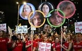 Des personnes brandissant des photos de cinq jeunes soldates prises en otage à Gaza, encadrées dans les cinq anneaux olympiques, lors d'une manifestation à Tel Aviv, le 27 juillet 2024. (Crédit : Ronaldo Schemidt/AFP)