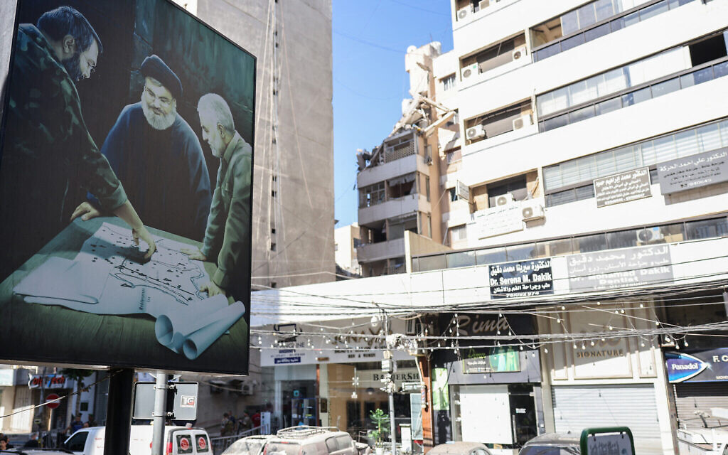 Un panneau d'affichage présentant une image de feu le chef de la Force Al-Qods iranienne Qassem Soleimani (à droite) et du chef du Hezbollah Hassan Nasrallah (au centre) face à un bâtiment visé par une frappe militaire israélienne sur un commandant du Hezbollah, à Beyrouth la veille, le 31 juillet 2024. (Crédit : Anwar Amro/AFP)