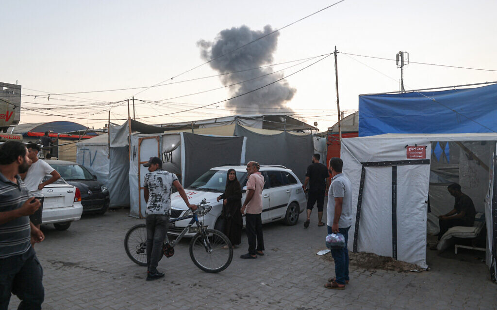 Des Palestiniens observant la fumée qui se dégage suite à une frappe israélienne, à Deir el-Balah, dans le centre de la bande de Gaza, le 6 août 2024 (Crédit : Eyad Baba/AFP)