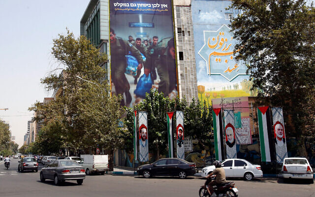 Un panneau d'affichage anti-Israël montrant des soldats israéliens en train de courir avec un slogan en hébreu qui se lit comme suit :  Même dans les abris, vous ne serez pas en sécurité et un autre en farsi qui se lit comme suit : Riez un peu maintenant, car vous pleurerez bientôt", sur un bâtiment de la place de Palestine à Téhéran, le 8 août 2024. (Crédit : AFP)