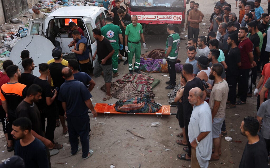 Des Palestiniens déplacés regardant les premiers intervenants se préparer à transporter les cadavres des personnes tuées lors d'une frappe israélienne sur une école, dans la ville de Gaza, le 10 août 2024. (Crédit : Omar al-Qattaa/AFP)