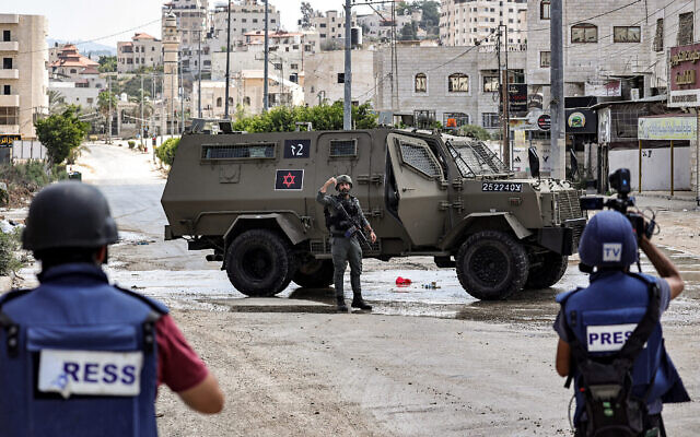Des journalistes filmant des véhicules de l'armée israélienne déployés à l'entrée de Tulkarem, lors d'un raid en cours, en Cisjordanie, le 22 août 2024. (Crédit : Zain Jaafar/AFP)