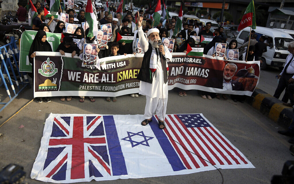 Un partisan du groupe musulman chiite pakistanais « Imamia Student Organization » et de la « Palestine Foundation Pakistan » se tenant sur des drapeaux britanniques, américains et israéliens à Karachi, au Pakistan, le 31 juillet 2024. (Crédit :Ikram Suri/AP)