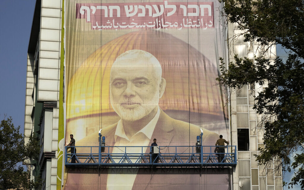Des ouvriers iraniens installant une énorme banderole sur un mur montrant un portrait du chef du groupe terroriste du Hamas, Ismaïl Haniyeh, et le sanctuaire islamique du Dôme du Rocher au sommet du mont du Temple à Jérusalem, avec une pancarte sur laquelle on peut lire en farsi et en israélien : « Attendez-vous à une punition sévère », sur la place de Palestine, à Téhéran, en Iran, le 31 juillet 2024. (Credit : Vahid Salemi/AP) Des ouvriers iraniens installant une énorme banderole sur un mur montrant un portrait du chef du groupe terroriste du Hamas, Ismaïl Haniyeh, et le sanctuaire islamique du Dôme du Rocher au sommet du mont du Temple à Jérusalem, avec une pancarte sur laquelle on peut lire en farsi et en israélien : « Attendez-vous à une punition sévère », sur la place de Palestine, à Téhéran, en Iran, le 31 juillet 2024. (Credit : Vahid Salemi/AP)