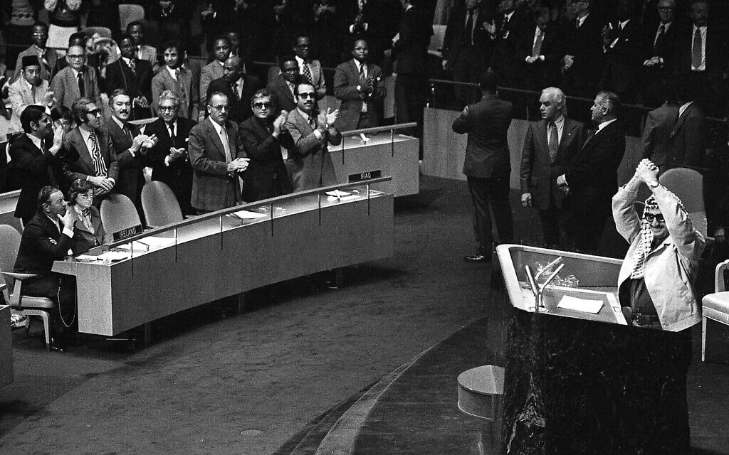 Yasser Arafat frappant des mains au-dessus de sa tête alors que certains délégués l'ovationnent, tandis que es deux délégués irlandais, assis au premier rang à gauche, restent assis, lors de l'Assemblée générale des Nations unies, à New York, le 14 novembre 1974. (Crédit : AP) Yasser Arafat frappant des mains au-dessus de sa tête alors que certains délégués l'ovationnent, tandis que es deux délégués irlandais, assis au premier rang à gauche, restent assis, lors de l'Assemblée générale des Nations unies, à New York, le 14 novembre 1974. (Crédit : AP)