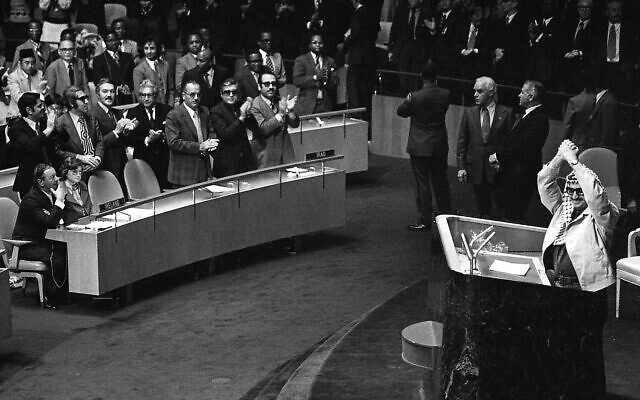 Yasser Arafat frappant des mains au-dessus de sa tête alors que certains délégués l'ovationnent, tandis que es deux délégués irlandais, assis au premier rang à gauche, restent assis, lors de l'Assemblée générale des Nations unies, à New York, le 14 novembre 1974. (Crédit : AP)