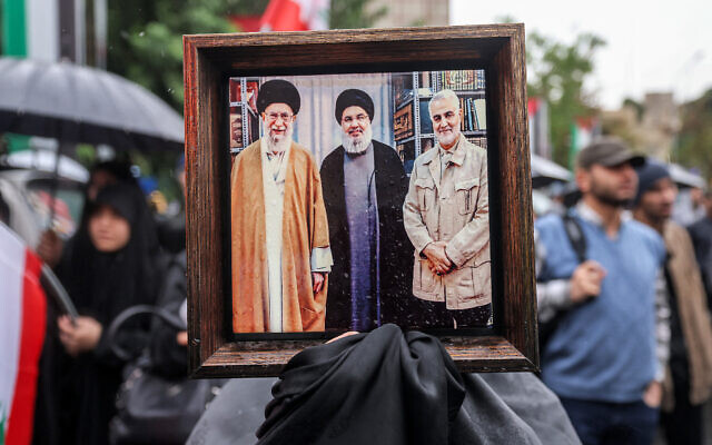 Un manifestant tenant une photo encadrée montrant (de gauche à droite) le guide suprême iranien Ali Khamenei, le chef du Hezbollah libanais Hassan Nasrallah, éliminé par une frappe aérienne israélienne le 27 septembre 2024, et le commandant de la Force Al-Qods du Corps des Gardiens de la Révolution islamique (CGRI) Qassem Soleimani, éliminé par une frappe de drone américaine en janvier 2020, lors d'une manifestation anti-Israël, sur la Place de Palestine, à Téhéran, le 28 septembre 2024. (Crédit : Atta Kenare/AFP)