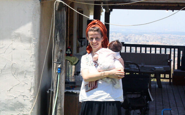 Tamar Ahituv, l'une des membres fondateurs de l'avant-poste illégal de Sde Ephraim en Cisjordanie, devant sa maison avec son bébé, le 8 juillet 2024. (Crédit : Jeremy Sharon/Times of Israel)