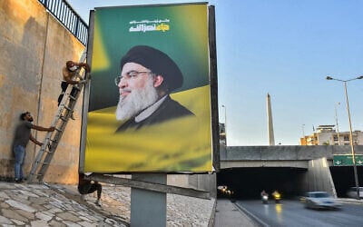 Des ouvriers accrochant des panneaux d'affichage portant le portrait du chef du groupe terroriste libanais Hezbollah, Hassan Nasrallah, tué, le long de l'autoroute de l'aéroport de Beyrouth, le 4 octobre 2024. (Crédit : Fadel Itani/AFP)
