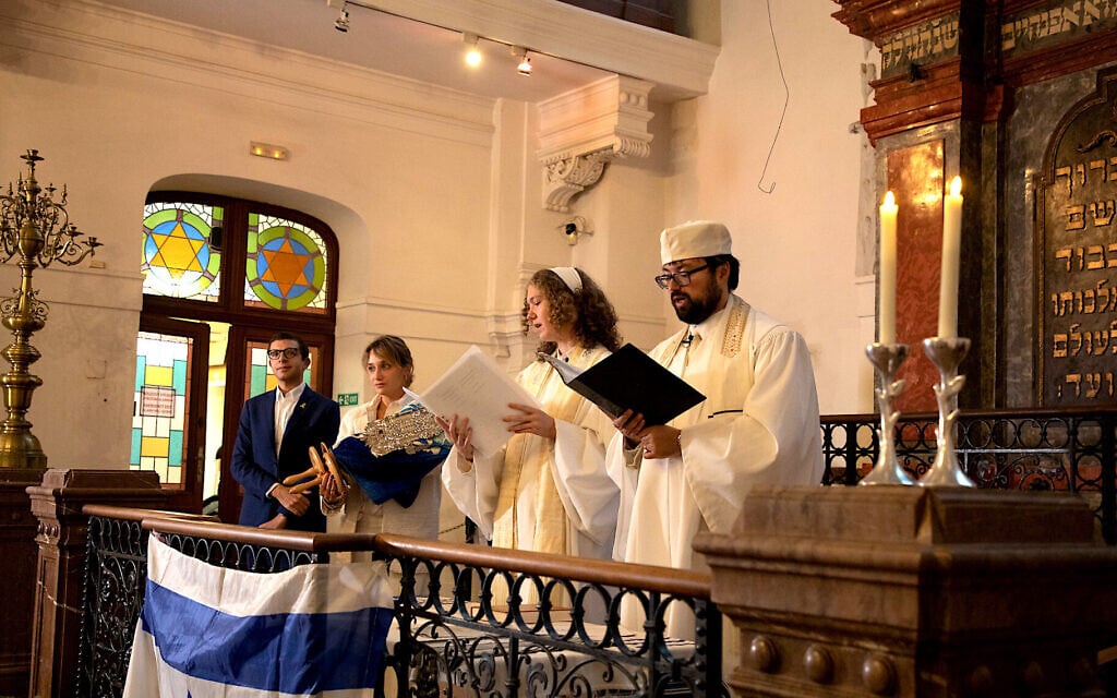 Le rabbin d'Ec Chajim David Maxa et une femme rabbin en cours de formation, Klára Kopytková, dirigent la prière de Kol Nidrei pendant l'office de Yom Kippour à la synagogue Klausen à Prague tandis que la présidente d'Ec Chajim, Anna Noskova, tient la Torah avec le vice-président de l'Union mondiale du judaïsme progressiste, Andrew Keene, le 11 octobre 2024. (Crédit : Dana Cabanova ; Autorisation : Musée juif de Prague) Le rabbin d'Ec Chajim David Maxa et une femme rabbin en cours de formation, Klára Kopytková, dirigent la prière de Kol Nidrei pendant l'office de Yom Kippour à la synagogue Klausen à Prague tandis que la présidente d'Ec Chajim, Anna Noskova, tient la Torah avec le vice-président de l'Union mondiale du judaïsme progressiste, Andrew Keene, le 11 octobre 2024. (Crédit : Dana Cabanova ; Autorisation : Musée juif de Prague)