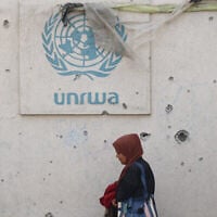 Une Palestinienne passant devant un mur endommagé portant le logo de l'UNRWA dans un camp de personnes déplacées, à Rafah, dans le sud de la bande de Gaza, le 28 mai 2024. (Crédit : Eyad Baba/AFP)