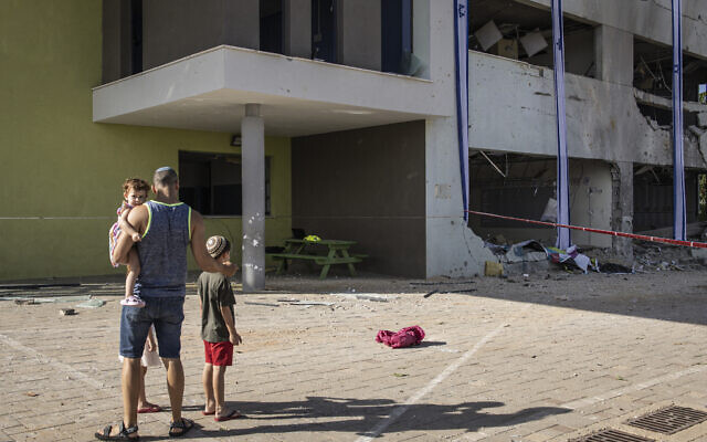 Un père montre à ses enfants une école qui a été touchée la veille par un barrage de missiles balistiques tirés sur Israël par l'Iran, dans la ville de Gedera, dans le sud d'Israël, le 2 octobre 2024. (JOHN WESSELS / AFP)