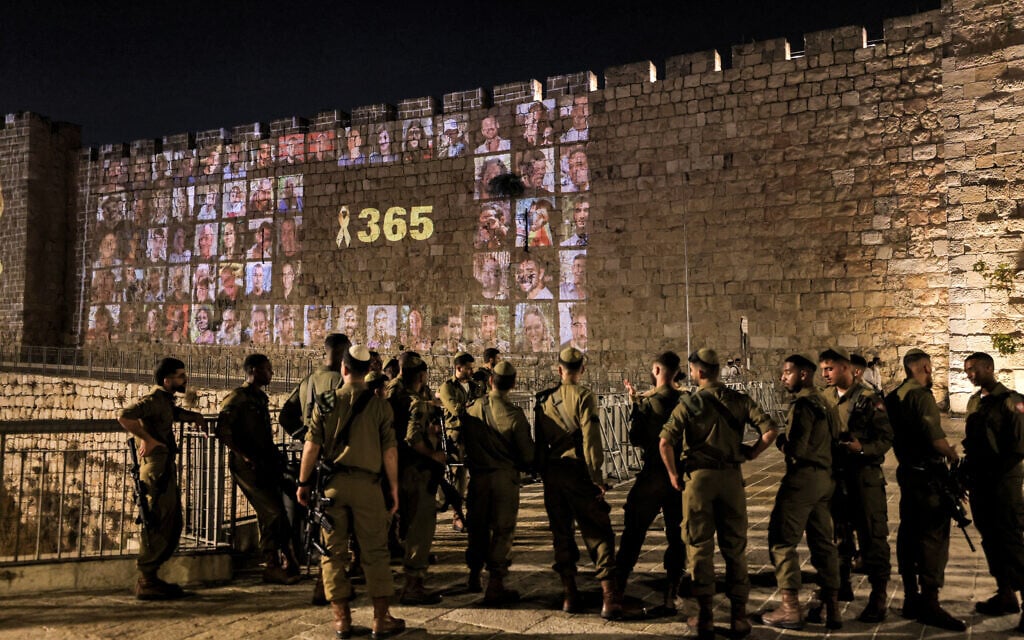 Des soldats de l'armée israélienne se tiennent debout alors qu'un ruban jaune portant le nombre 365, signifiant le nombre de jours écoulés depuis les attaques du 7 octobre 2023 menées par le Hamas, est projeté avec des photos des victimes des attaques le long des murs de la Vieille ville de Jérusalem, le 6 octobre 2024, à la veille du premier anniversaire de la guerre qui a été déclenchée par les attaques. (Crédit : AHMAD GHARABLI / AFP) Des soldats de l'armée israélienne se tiennent debout alors qu'un ruban jaune portant le nombre 365, signifiant le nombre de jours écoulés depuis les attaques du 7 octobre 2023 menées par le Hamas, est projeté avec des photos des victimes des attaques le long des murs de la Vieille ville de Jérusalem, le 6 octobre 2024, à la veille du premier anniversaire de la guerre qui a été déclenchée par les attaques. (Crédit : AHMAD GHARABLI / AFP)