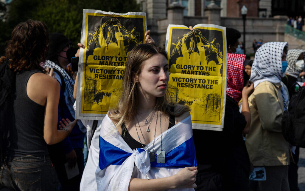 Des manifestants anti-israéliens brandissent des affiches derrière une étudiante participant à un rassemblement de commémoration des victimes du 7 octobre 2023 à l'occasion du premier anniversaire du pogrom du Hamas à New York, le 7 octobre 2024. (Crédit : Alex Kent / GETTY IMAGES NORTH AMERICA / Getty Images via AFP)
